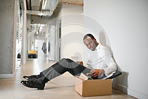Portrait shot of African American sad businessman in suit and tie sitting with box of stuff. Male office worker lost job