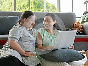 Portrait shot of Asian lovely mother sitting on floor and young chubby down syndrome autistic autism little daughter lay down on
