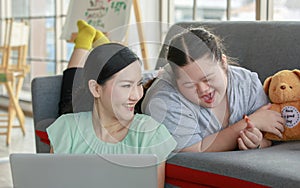 Portrait shot of Asian lovely mother sitting on floor and young chubby down syndrome autistic autism little daughter lay down on