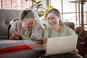 Portrait shot of Asian lovely mother sitting on floor and young chubby down syndrome autistic autism little daughter lay down on