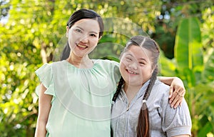 Portrait shot of Asian mother and young chubby down syndrome autistic autism little cute girl with braid pigtail hairstyle stand