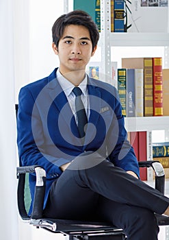Portrait shot of Asian young friendly smart law student wears blue formal suit and tie stand leaning wall hold hands in pockets