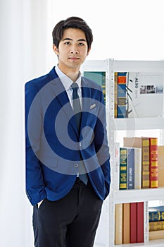 Portrait shot of Asian young friendly smart law student wears blue formal suit and tie stand leaning wall hold hands in pockets