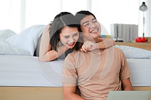Portrait shot of cute smiling young Asian lover couple in casual clothes relax at home on weekends. The wife lies on the bed