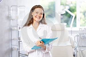 Portrait shot of doctor holding clipboard in hand while standing in medical esthetic office