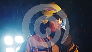 Portrait shot of a fireman in action speaking on the walkie talkie. Fire reflection on the helmet and reflectors in the