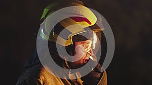 Portrait shot of a fireman in action speaking on the walkie talkie. Fire reflection on the helmet. Slow motion