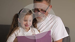 Portrait shot of the grandfather in glasses and cute teen granddaughter reading a book together while sitting on the