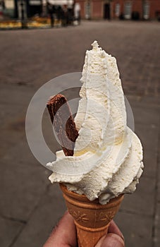 Portrait shot of a hand held whipped ice cream with a chocolate flake sticking out the side,  against a plain