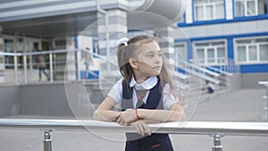 Portrait shot of the pretty little girl in the school uniform in the school yard against the building of a primary