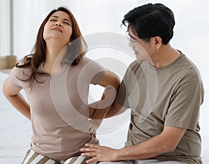 Portrait shot of senior Asian lover couple wearing eyeglasses. Wife suddenly feels uncomfortable from the back pain with a worried