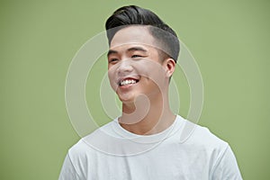 Portrait shot of young adult Asian man smiling posturing on green wall background