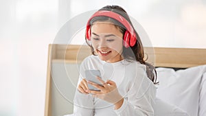 Portrait shot of a young adult Asian woman in casual white clothes using a digital smartphone to search for the popular music