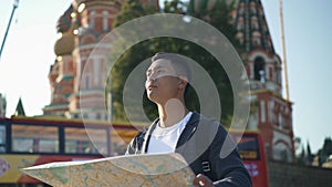 Portrait shot of a young Asian man looking at map. The Cathedral of Vasily the Blessed on background, Moscow Russia. Red