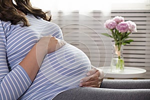 Portrait shot of young beautiful woman on third trimester of pregnancy. Close up of pregnant female with arms on her round belly.