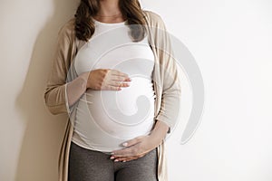 Portrait shot of young beautiful woman on third trimester of pregnancy. Close up of pregnant female with arms on her round belly.
