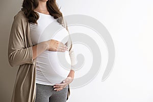 Portrait shot of young beautiful woman on third trimester of pregnancy. Close up of pregnant female with arms on her round belly.