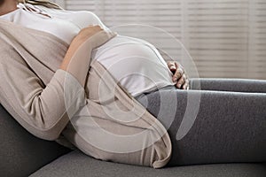 Portrait shot of young beautiful woman on third trimester of pregnancy. Close up of pregnant female with arms on her round belly.