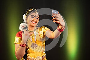 Portrait shot of Young girl in Bharatnatyam dancer costume taking selfie on mobile phone - concept of social media