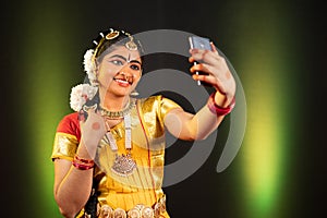 Portrait shot of Young girl in Bharatnatyam dancer costume taking selfie on mobile phone - concept of social media photo
