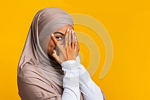 Portrait of shy black muslim girl in headscarf peeking through fingers