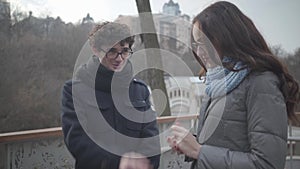 Portrait of shy Caucasian boyfriend and girlfriend in eyeglasses laughing and talking in autumn park. Nerd boy and girl