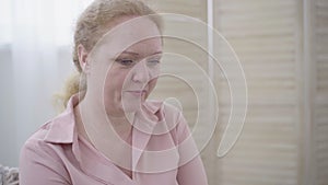 Portrait of shy senior woman looking at camera and smiling. Pretty aged Caucasian lady posing indoors. Lifestyle