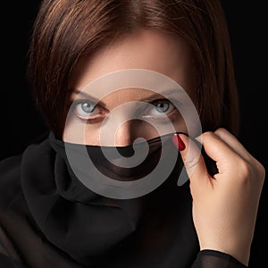 Portrait of shy woman covering her mouth and nose or face with scarf and looking at camera