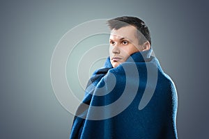 Portrait of a sick man with flu, allergy, germs, cold. Wrapped In a blanket against a light background