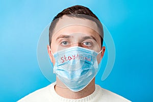 Portrait of a sick man wearing medical mask with Stay home text at blue background. Coronavirus self isolation concept. Protect