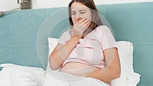 Portrait of sick pregnant woman feeling nausea and coughing while lying in bed at morning. Healthcare and intoxication