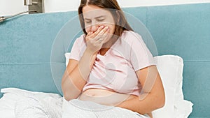 Portrait of sick pregnant woman feeling nausesa and coughing while lying in bed at morning. Healthcare and intoxication