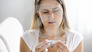 Portrait of sick woman with flu looking on digital thermometer after measuring temperature
