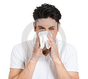 portrait of sick young man with allergy or germs cold, blowing his nose looking miserable unwell very sick, isolated on white