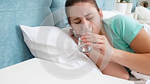 Portrait of sick young woman lying in bed and drinking water from glass