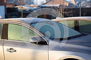 A portrait of the side of a car with frozen side windows and a frozen windshield during winter. The ice first needs to melt or be