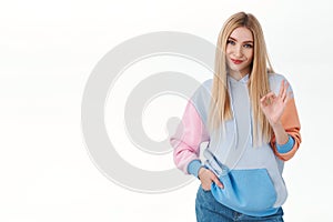 Portrait of silly good-looking blond girl with pleased smile, showing okay sign and nod in approval, agree, give