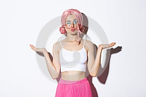Portrait of silly pop girl wearing pink wig, winking at camera while holding something in both hands, standing over