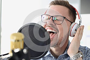 Portrait of singing young man in headphones front of microphone in studio
