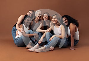 Portrait of six laughing women of different ages and body types sitting together on a brown background in studio