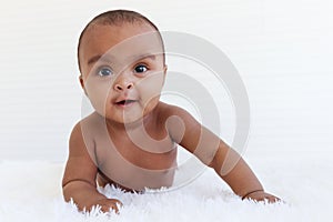 Portrait of a six month crawling African American baby on fluffy white rug, happy smiling adorable sweet little girl kid lying on