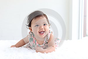 Portrait of a six months crawling baby on fluffy white rug, happy smiling adorable sweet little girl kid lying on bed in bedroom,