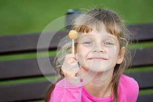 Portrait of a six-year-old cheerful girl who holds a lollipop in her hand