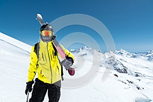 A portrait of a skier in a protective helmet and glasses is a mask and scarf with skis on his shoulder in the snow