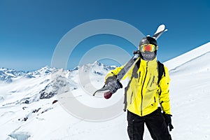 A portrait of a skier in a protective helmet and glasses is a mask and scarf with skis on his shoulder in the snow