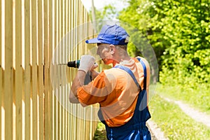 Portrait of skilled worker building wooden fence with cordless electric screwdriver