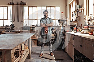 Skilled young woodworker standing in his workshop full of tools photo