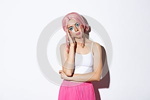 Portrait of sleepy cute girl looking bored at halloween party, wearing pink wig and skirt, standing unamused over white