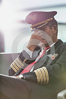 Portrait of sleepy and overworked pilot sitting in airport