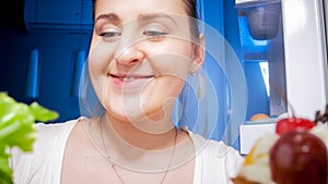 Portrait of young sleepy woman looking for something to eat in refrigerator